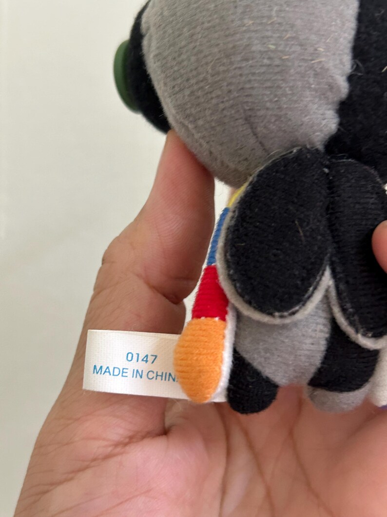 May include: A plush toy with a gray head and black wings. The toy has a colorful tail with red, yellow, and blue accents. A tag reads "0147 MADE IN CHIN".