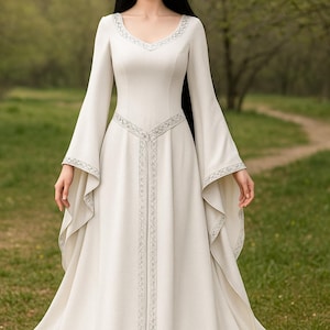 May include: A long, ivory-colored dress with long, flowing sleeves. The dress features a V-neckline and is adorned with silver embroidered detailing along the neckline, sleeves, and bodice. The dress is suitable for a wedding or special occasion.