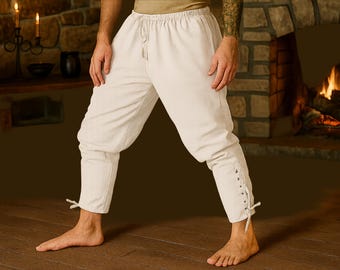 May include: Off-white, medieval-style pants with a drawstring waist and gathered knees. The lower legs feature a lace-up detail and tie closure. The pants are made of a soft, light-colored fabric.