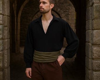 May include: A black long-sleeve shirt with a V-neck, paired with brown pants and a green sash. The outfit is reminiscent of historical or theatrical attire. The pants have visible buttons.