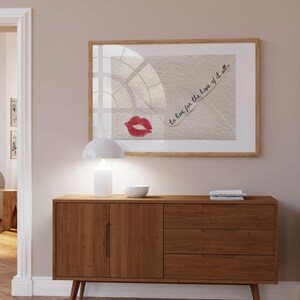 May include: A wooden cabinet with two doors and three drawers. The cabinet is a light brown color and has a modern design. A framed print with the text "to live for the hope of it all." is hanging on the wall above the cabinet.