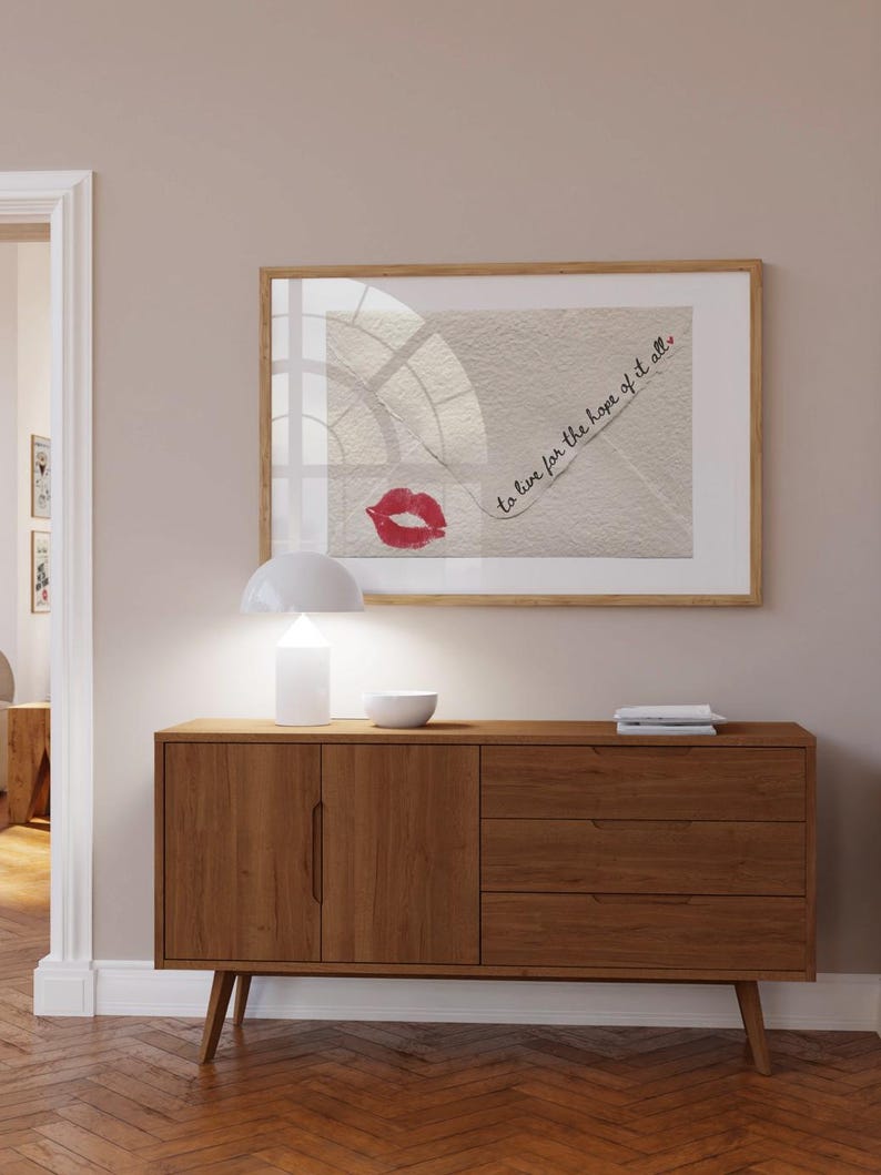 May include: A wooden cabinet with two doors and three drawers. The cabinet is a light brown color and has a modern design. A framed print with the text "to live for the hope of it all." is hanging on the wall above the cabinet.