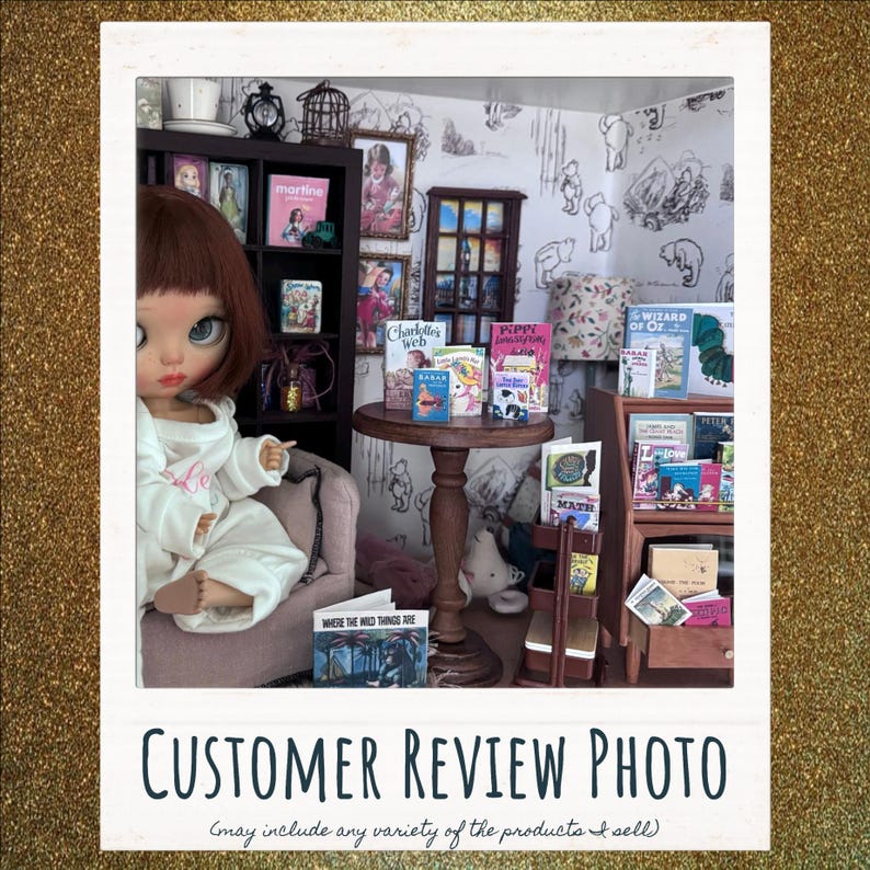 May include: A miniature dollhouse scene featuring a doll with auburn hair in a white outfit sitting in a chair. The room includes a dark wooden bookshelf, a round pedestal table with miniature books, and a wooden display stand filled with tiny books.