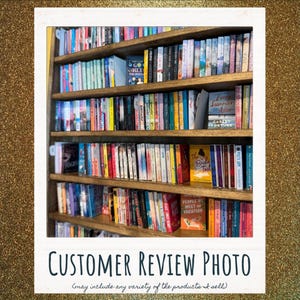 May include: A tall wooden bookshelf filled with numerous books arranged in rows. The spines display a variety of colors, titles, and authors. Some books are positioned with their front covers facing forward, including titles like Go Hex Yourself.