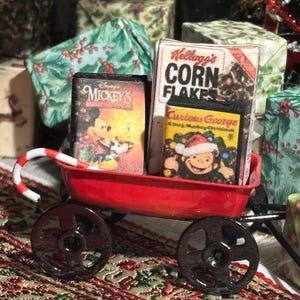 Pu&ograve; includere: Un carretto rosso in miniatura in metallo che trasporta una scatola di Kellogg's Corn Flakes, una videocassetta di Mickey's Christmas Carol e una di Curious George A Very Monkey Christmas, con un bastoncino di zucchero sul bordo.