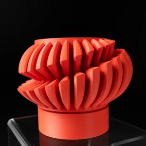 May include: A bright orange ceramic planter with a unique, geometric design. The planter has a wide, round base and a textured, ruffled top.
