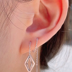 May include: A pair of silver earrings with a diamond-shaped pendant and a chain that hangs down from the earlobe.