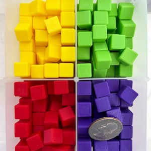 May include: A clear plastic container divided into four sections, each filled with small, colourful cubes. The cubes are yellow, green, red, and purple. A coin is included for size reference.