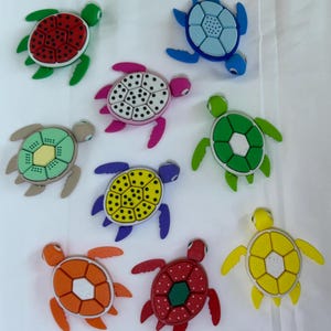 May include: Nine colorful plastic turtle toys with different patterns on their shells. The turtles are in various colors, including red, green, blue, yellow, orange, purple, and white.