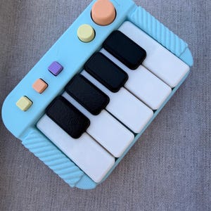 May include: A light blue toy piano with black and white keys. The toy has a series of colored buttons and a large orange knob. The piano is a miniature version of a keyboard instrument.