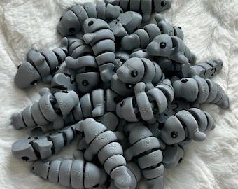 May include: A pile of gray, segmented, plastic toys resembling fish. The toys have black eyes and are arranged in a random pattern.