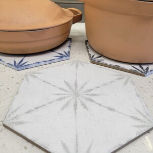Puede incluir: Dos ollas de terracota con tapas colocadas sobre trípodes hexagonales de cerámica blanca con diseños geométricos azules y blancos. Los trípodes tienen un patrón de estrella.