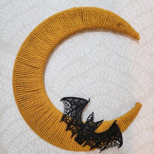 May include: A yellow crescent moon-shaped wreath with a black lace bat attached to it.