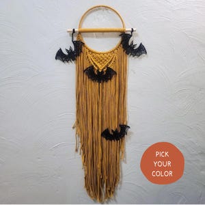 May include: A macrame wall hanging with a circular wooden hoop and black bat cutouts. The macrame is made with yellow yarn and has a fringe at the bottom. The text "PICK YOUR COLOR" is visible in the lower right corner of the image.