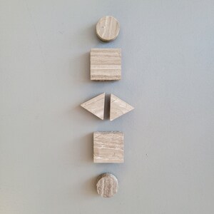 May include: A set of five geometric shapes made of light brown stone. The shapes are a circle, a square, two triangles, and another circle. The shapes are arranged vertically in a line.