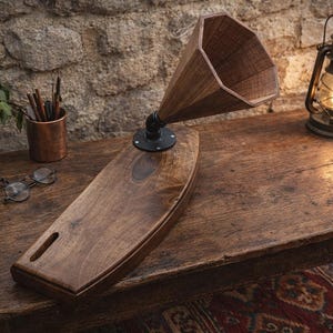 Può includere: Un amplificatore acustico in legno per smartphone con finitura marrone scuro, una tromba geometrica ottagonale e una base in raccordo metallico nero. Il dispositivo è realizzato in legno e include una fessura per inserire lo smartphone.