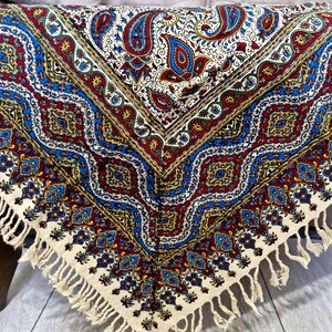 May include: A white tablecloth with a colorful paisley pattern in shades of blue, red, yellow, and green. The tablecloth has a fringe border.