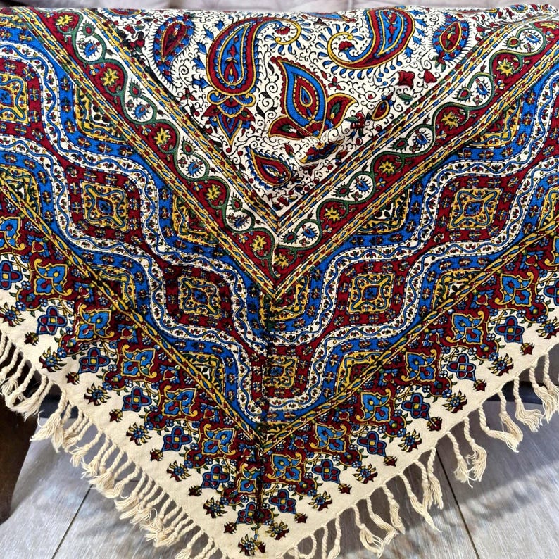 May include: A white tablecloth with a colorful paisley pattern in shades of blue, red, yellow, and green. The tablecloth has a fringe border.