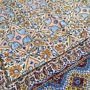 May include: A detailed textile with a repeating pattern of floral and bird motifs in shades of blue, orange, and pink on a cream background. The border features a paisley design with blue and gold accents.