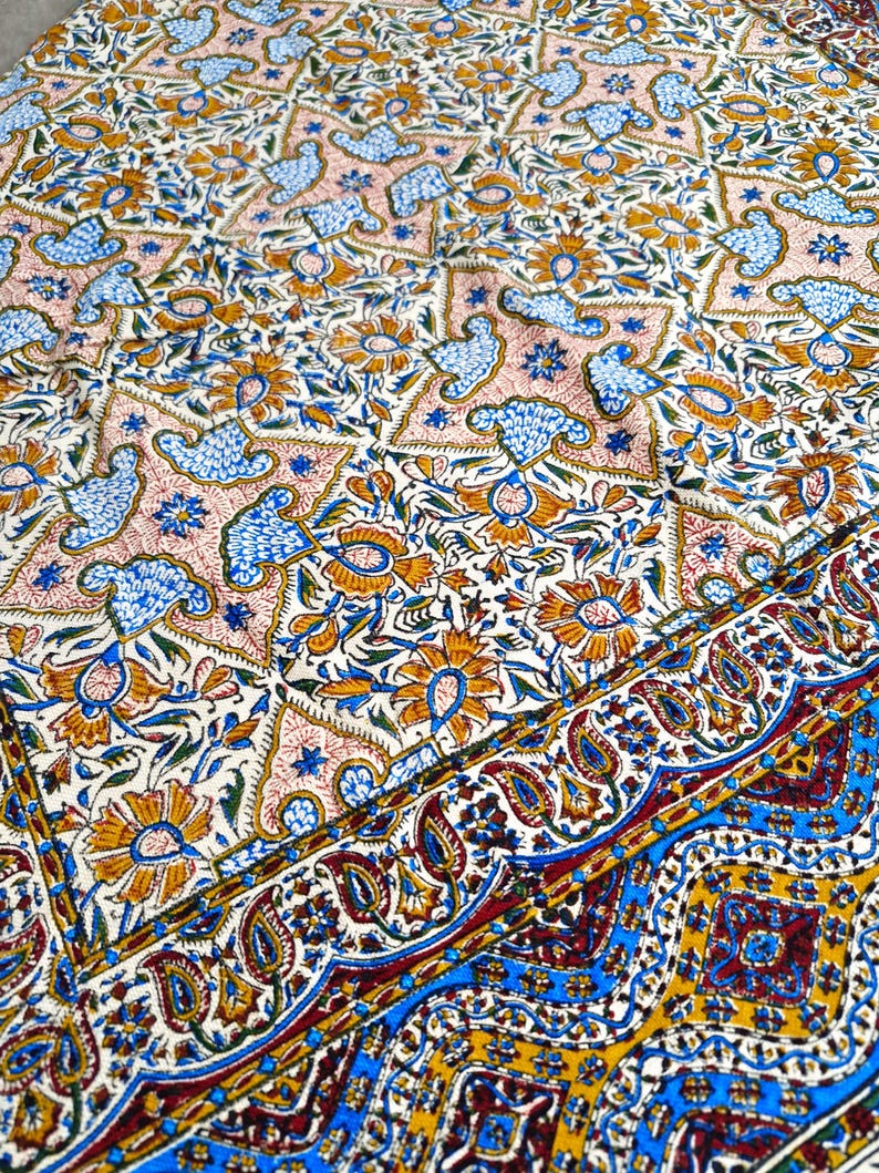 May include: A detailed textile with a repeating pattern of floral and bird motifs in shades of blue, orange, and pink on a cream background. The border features a paisley design with blue and gold accents.