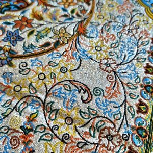 May include: Close-up of a white fabric with a colorful floral pattern. The fabric has a shiny, glittery texture. The pattern includes blue, green, orange, and yellow flowers.