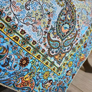 May include: A blue and gold patterned tablecloth with a paisley design. The tablecloth has a fringed edge and is made of a soft, luxurious fabric.