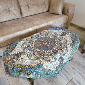 May include: A round, blue and white table cover with a floral and paisley design. The table cover is on a coffee table in front of a brown couch.
