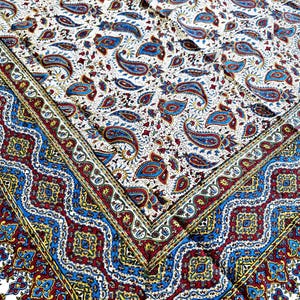 May include: A white tablecloth with a paisley pattern in shades of blue, red, and yellow. The tablecloth has a border with a repeating pattern of blue, red, and yellow.