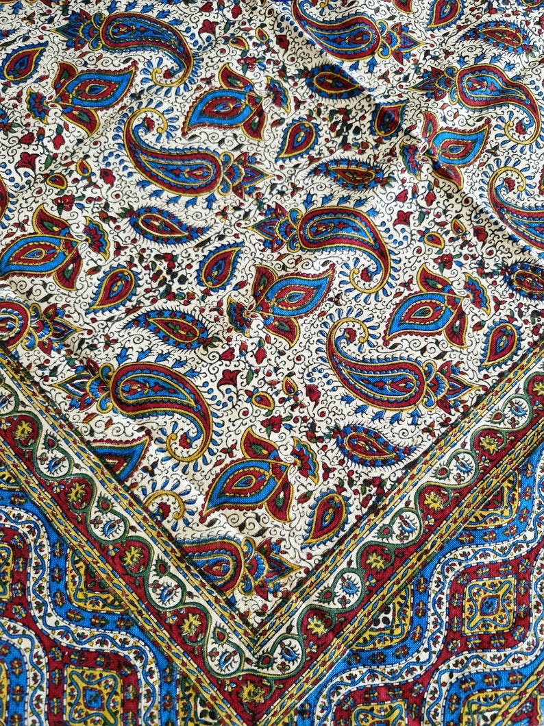 May include: A white fabric with a paisley pattern in shades of blue, red, and gold. The fabric has a border with a repeating pattern of blue, red, and gold.