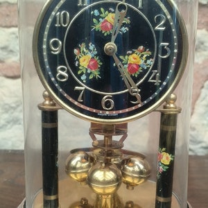 May include: A vintage, black-faced pendulum clock with a floral design on the face. The clock is encased in a glass dome and sits on a black base with a gold trim.