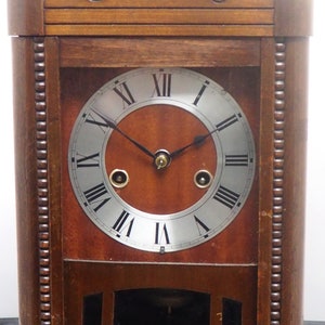 May include: A wooden antique clock with a Roman numeral face and a pendulum. The clock has a dark brown finish and ornate details.