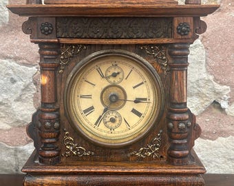 May include: Antique wooden alarm clock with intricate carvings and a round, white face with black Roman numeral markings. The clock has a brass trim and a small, round, white face with black markings for the seconds.