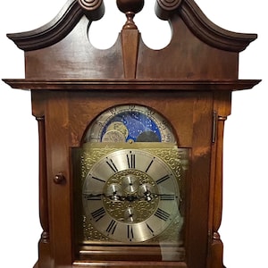 May include: A wooden grandfather clock with a gold face and a moon phase dial. The clock has a decorative top with a finial.