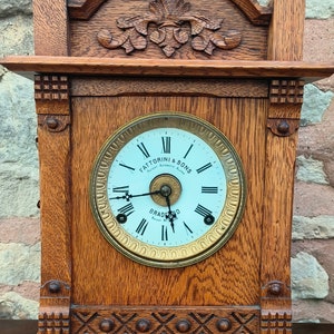 May include: Antique wooden clock with a white face and gold trim. The clock face reads "Fattorini & Sons Patent Automatic Alarm Bradford Patent No. 123456".