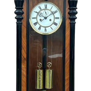May include: Antique wooden wall clock with black accents, a white face, and gold Roman numeral hour markers. The clock has a glass front and a pendulum with two weights.