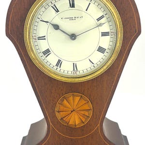 Puede incluir: Un reloj de chimenea de madera con una esfera dorada y números romanos. La esfera del reloj dice "E. Johnson & Co. Ltd. Dublin".