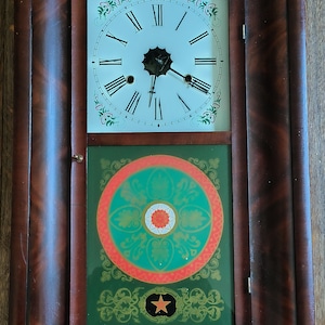 May include: Antique wooden clock with a white face and Roman numeral hour markers. The clock has a green and red painted design with a gold star.
