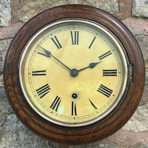 Op de afbeelding: Een vintage houten wandklok met Romeinse cijfers op de wijzerplaat. De klok heeft een donkerhouten frame en een glazen kap over de wijzerplaat.
