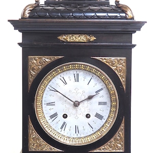 May include: A black and gold mantle clock with ornate details and a white face with Roman numerals.