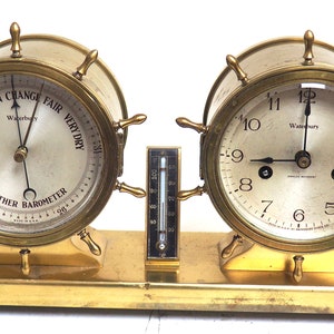Könnte beinhalten: Messing-Uhr- und Barometer-Set mit Schiffsrad-Design. Das Zifferblatt der Uhr zeigt "Waterbury" und das Zifferblatt des Barometers zeigt "Waterbury Weather Barometer".