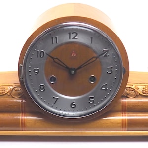 May include: A wooden mantel clock with a silver face and black hands. The clock has a carved wooden base with a floral design.