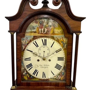 Puede incluir: Un reloj de pie antiguo de madera alto con una esfera blanca y marcadores de hora romanos negros. La esfera del reloj tiene una escena pintada de un guerrero escocés y una inscripción pintada que dice "Jas: Aitken, Glasgow."
