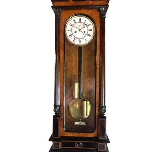 Puede incluir: Un reloj de abuelo antiguo de madera con una esfera redonda. El reloj tiene un péndulo y un peso de color latón. La madera tiene un acabado oscuro y rico con detalles decorativos. Una pieza clásica de decoración del hogar.
