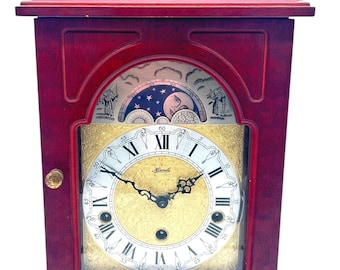 Könnte beinhalten: Eine Kaminuhr aus Mahagoniholz mit einem goldenen Zifferblatt und römischen Ziffern für die Stunden. Die Uhr hat ein Mondphasen-Zifferblatt mit einer Darstellung von Mond und Sternen. Das Zifferblatt der Uhr zeigt "Hermle".