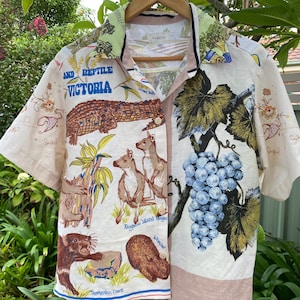 May include: A cream-coloured short-sleeved shirt with a button-down design. The shirt features a print of Australian animals, including a crocodile, kangaroos, and a Tasmanian devil, with the text "AND REPTILE VICTORIA". A grape design is also present.