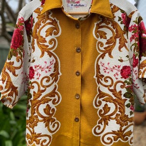 May include: A short-sleeved button-down shirt featuring a mustard yellow centre panel and collar, contrasted by white side panels with a brown scrollwork pattern and red floral accents. The interior label displays the text notrotnew and size L.