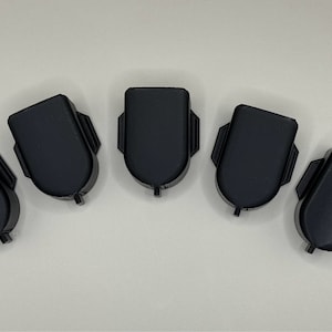 Puede incluir: Cinco tapones de plástico negro con la parte superior redondeada y la parte inferior plana. Los tapones tienen una superficie ligeramente texturizada.