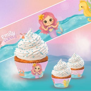 Puede incluir: Cupcakes con glaseado blanco y chispas azules, decorados con envoltorios temáticos de sirenas. Los envoltorios presentan ilustraciones de sirenas, cangrejos e hipocampos. El texto "Emily Turns 6" es visible.