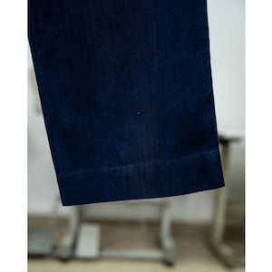 May include: Close-up of a section of dark blue denim pants. The fabric has a slight sheen, and the hem is visible at the bottom. The pants appear to be a wide-leg style.
