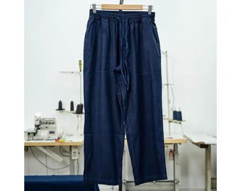 Può includere: Un paio di pantaloni casual blu scuro con vita a coulisse. I pantaloni sono appesi a un appendiabiti in legno.